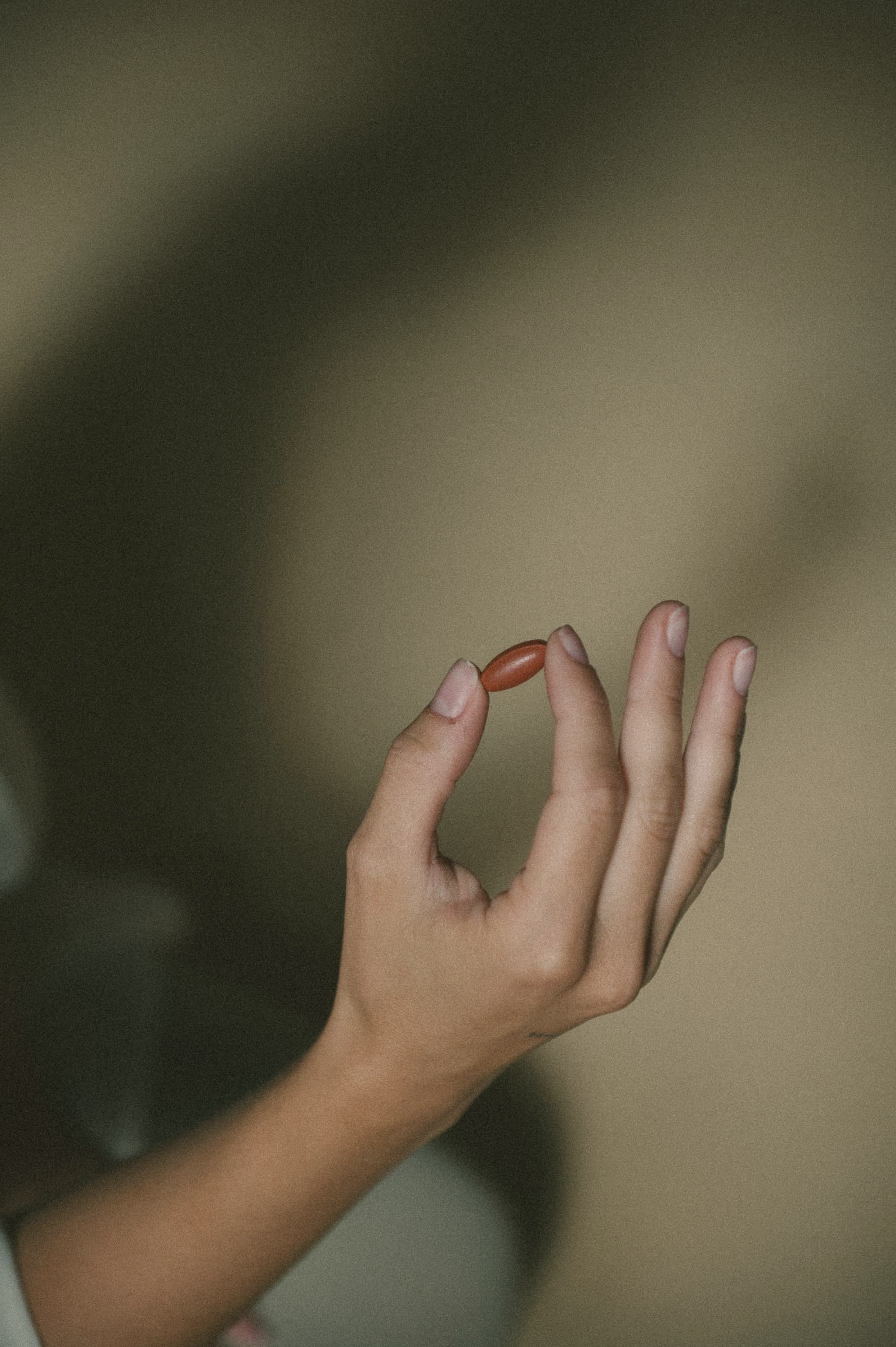A hand holding a single red tablet between finger and thumb