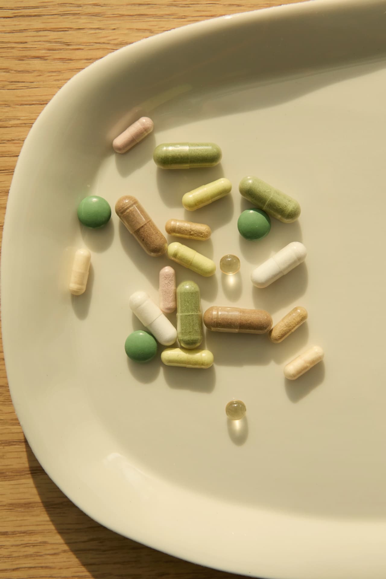 Capsules and tablets in soft colours on a cream plate, in sunlight