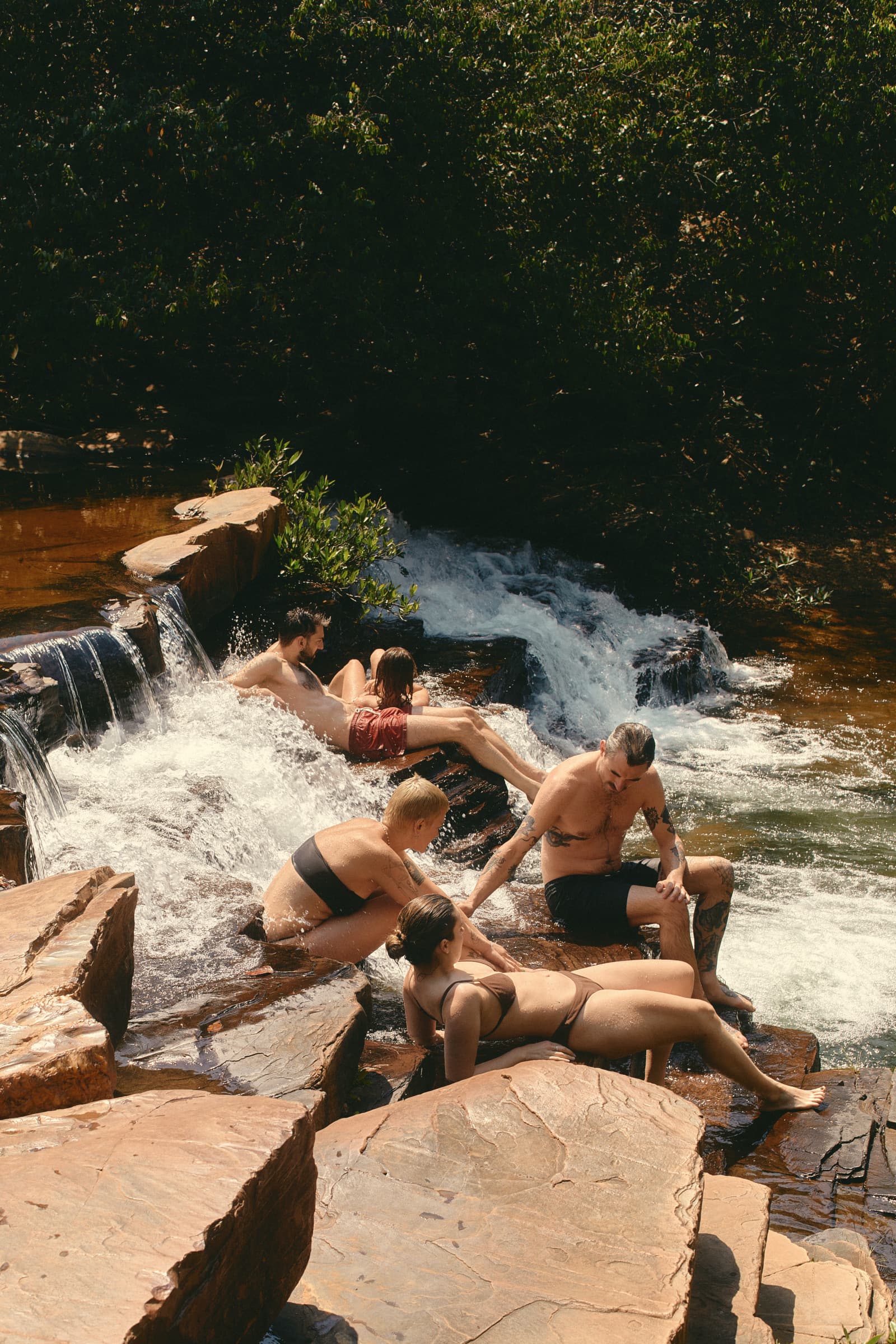 Friends lying back on the rocks of a waterfall, the water rushing past them