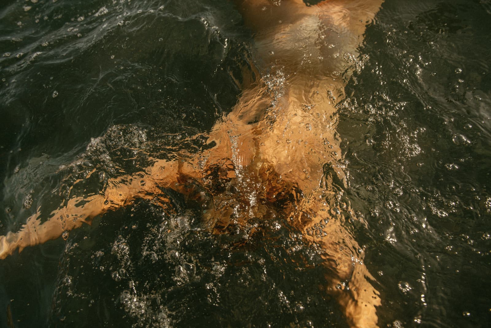 A swimmer under dark water, lit gold by the sun